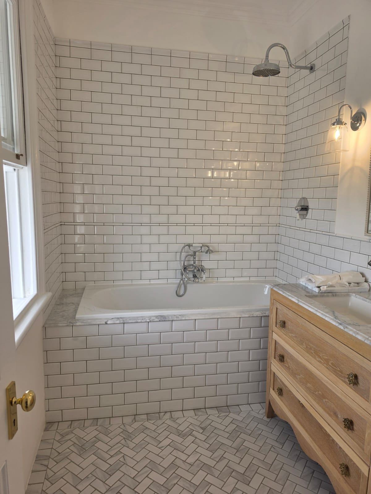 Finished bathroom with subway-tiled bath surround, marble sill and herringbone marble floor