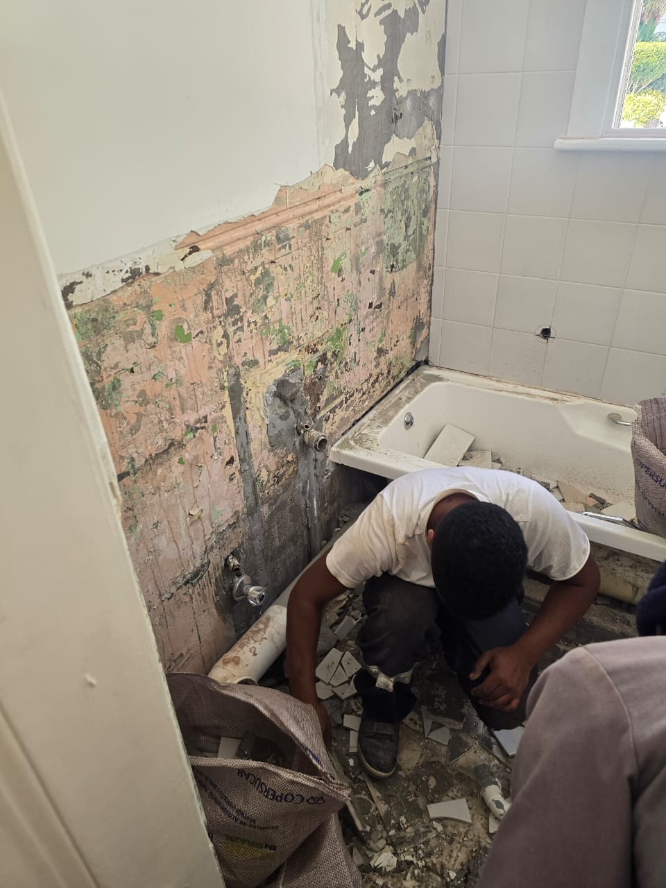 Bathroom wall stripped back to damp brickwork with old plumbing exposed before re-tiling