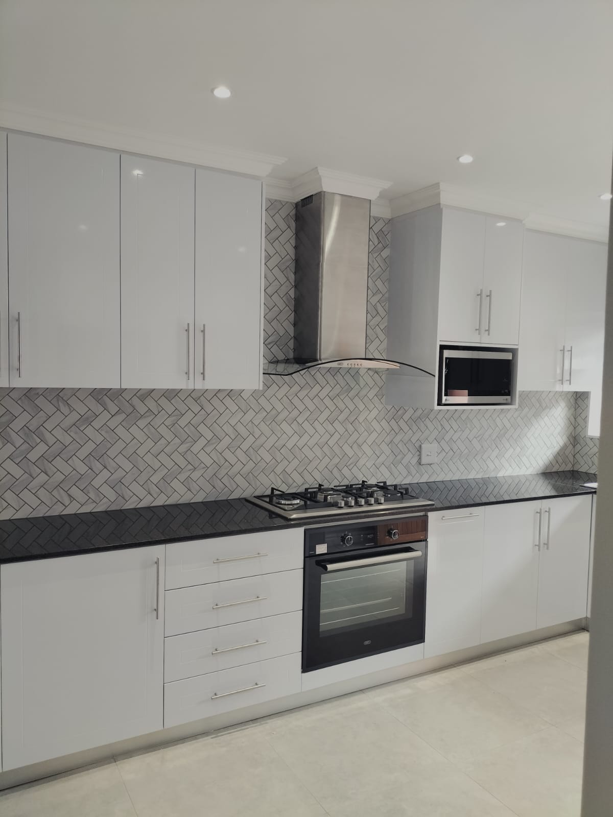 Finished kitchen with gloss white cabinetry, herringbone splashback tiling, granite worktop and gas hob