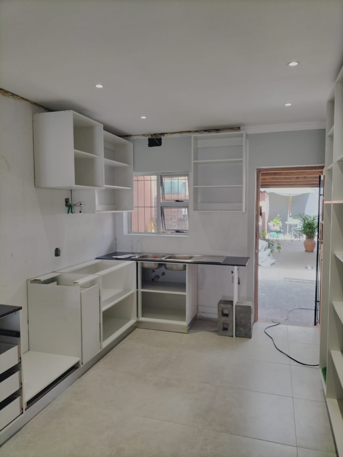 Kitchen mid-renovation with bare white cabinet carcasses, no splashback or worktop yet fitted