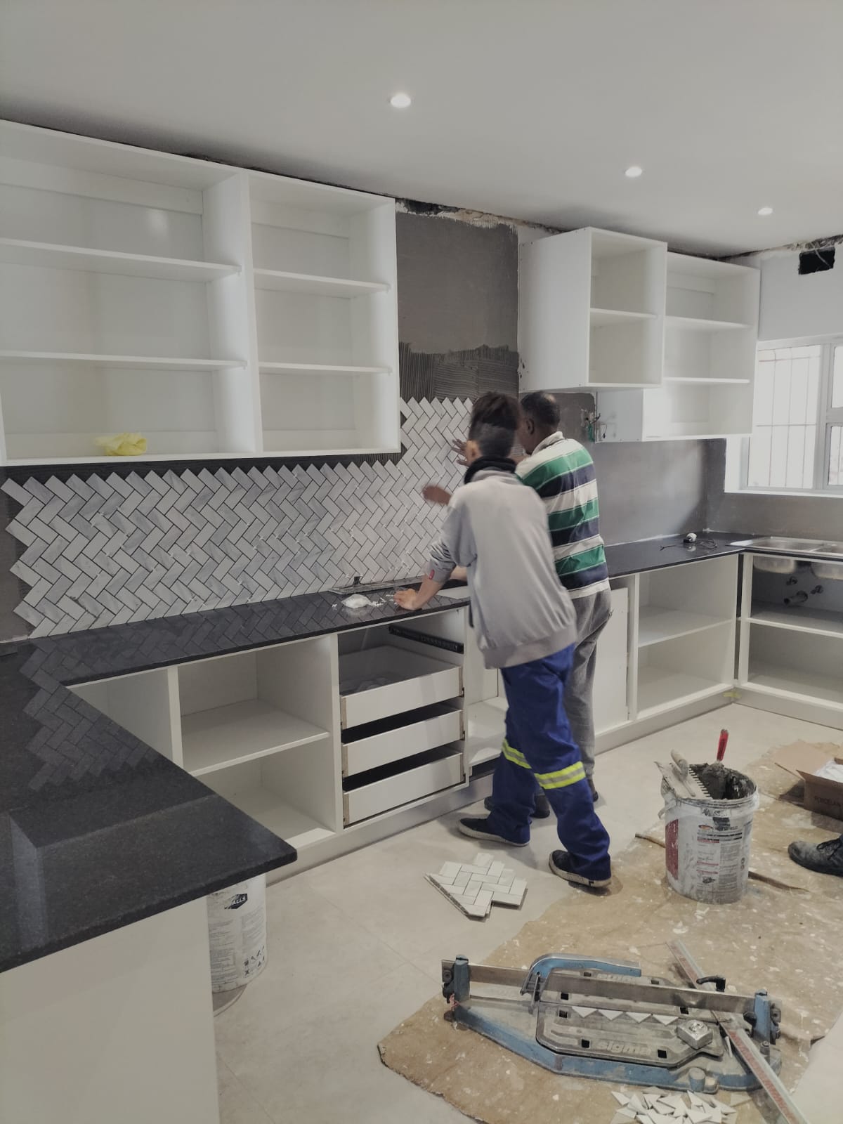 Tilers setting a herringbone marble splashback in place over a fitted granite worktop