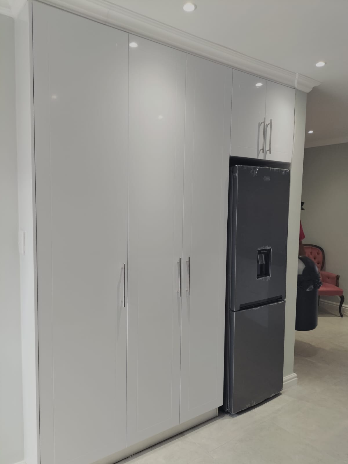 Floor-to-ceiling gloss white pantry cabinetry with an integrated fridge-freezer