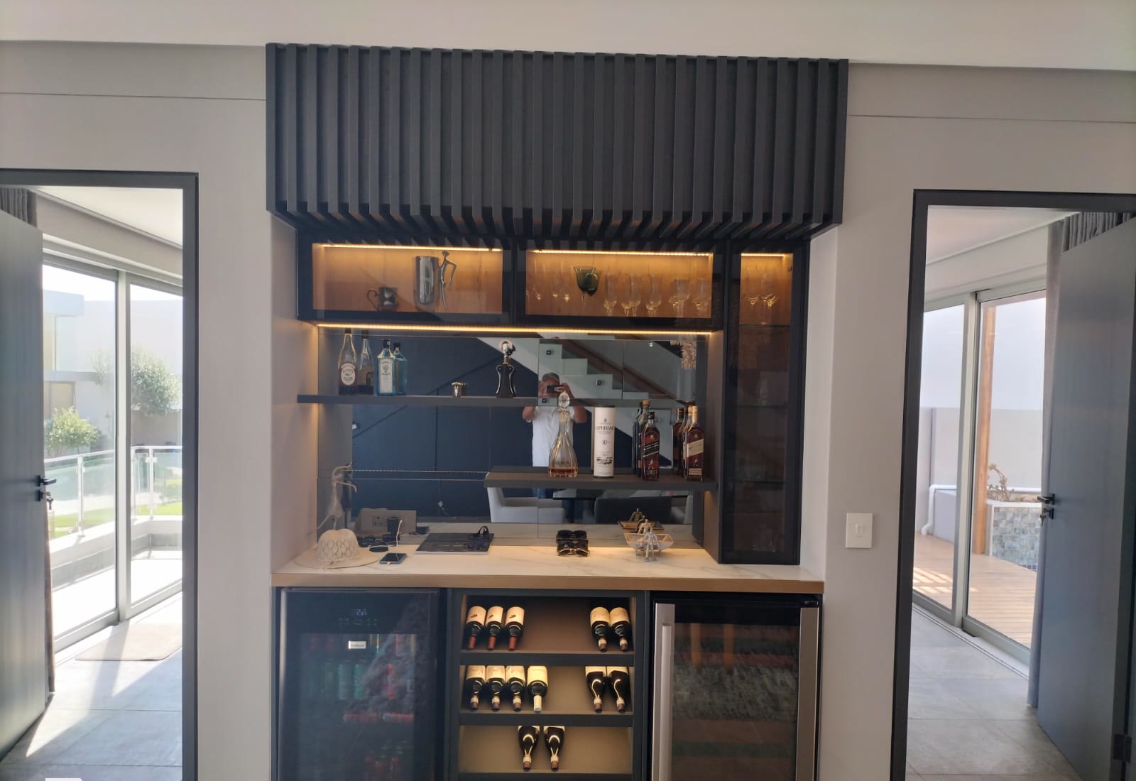 Custom home bar with a fluted timber-look bulkhead, stone counter and integrated wine coolers
