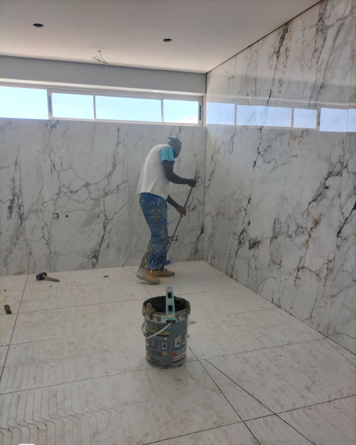 Installer setting large-format marble-effect floor tiles beneath a matching book-matched wall cladding
